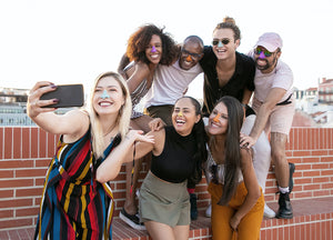 A group of 7 various aged young people of different ethnic backgrounds and skin colors.  Each wearing one of the four fun colors of Noz sunscreen on their noses.